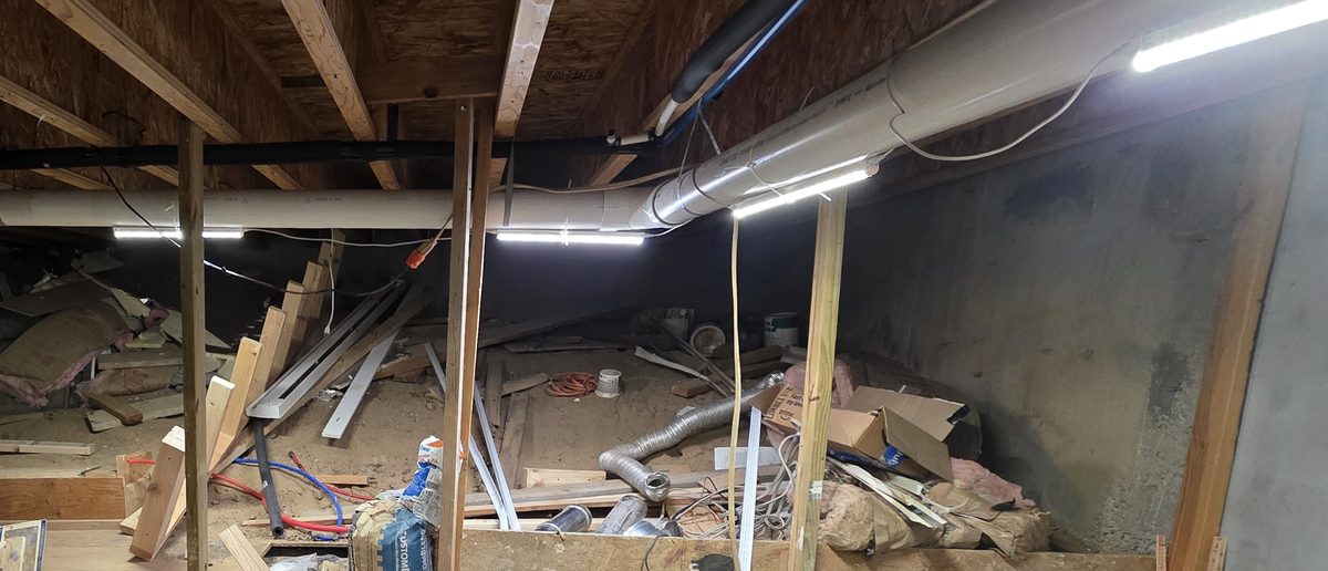 Before: wide view of the basement with boxes, buckets, bins and lumber piled under the joists